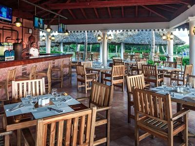 Offenes Restaurant mit Holzmöbeln, gedeckten Tischen und Blick auf grünen Garten.