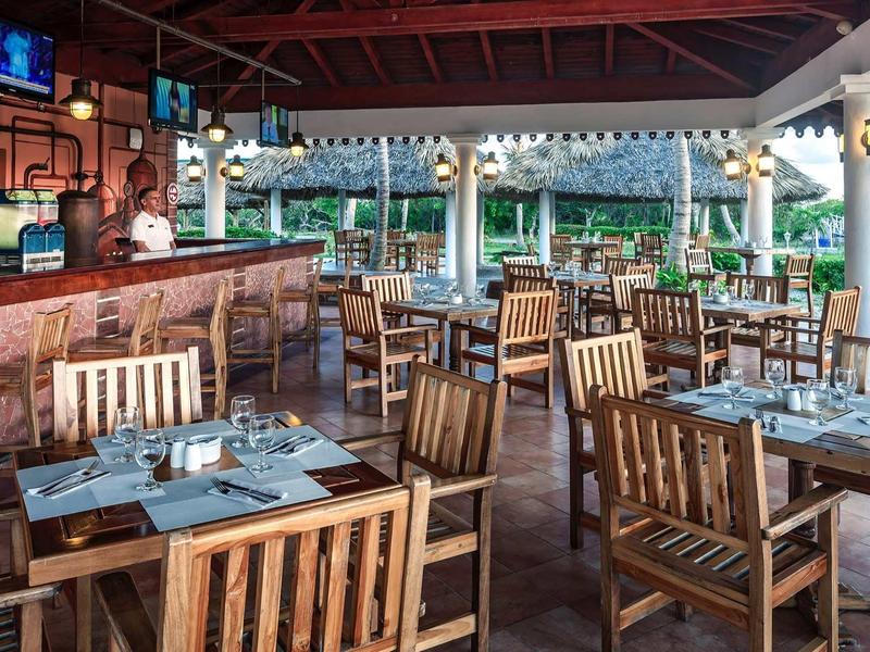 Offenes Restaurant mit Holzmöbeln, gedeckten Tischen und Blick auf grünen Garten.