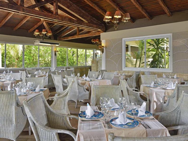 Ein helles, offenes Restaurant mit Holzdach, weißen Stühlen und Tischen, mit gedeckter Tischwäsche.