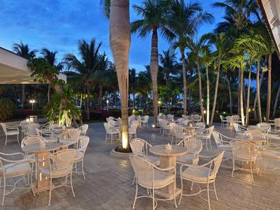 Outdoor-Terrassenbereich mit weißen Tischen und Stühlen unter Palmen bei Abenddämmerung.