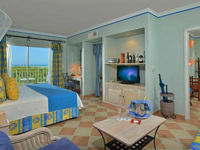 Hell eingerichtetes Hotelzimmer mit Balkon, Meerblick, Doppelbett, Sofa und Tisch.