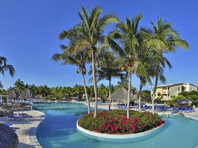 Großer Pool mit Palmeninsel, blauer Wasserfläche und Sonnenschirmen in sonnigem Resort.