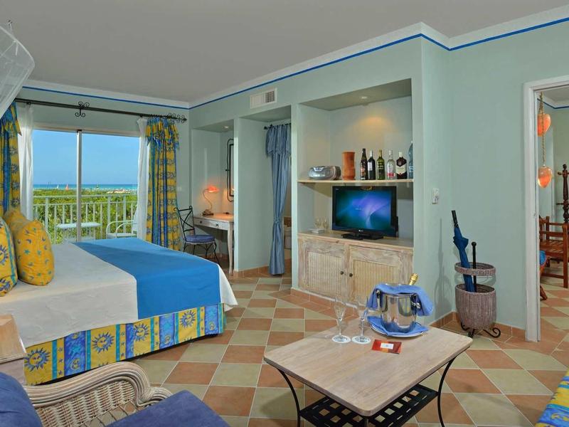 Hell eingerichtetes Hotelzimmer mit Balkon, Meerblick, Doppelbett, Sofa und Tisch.