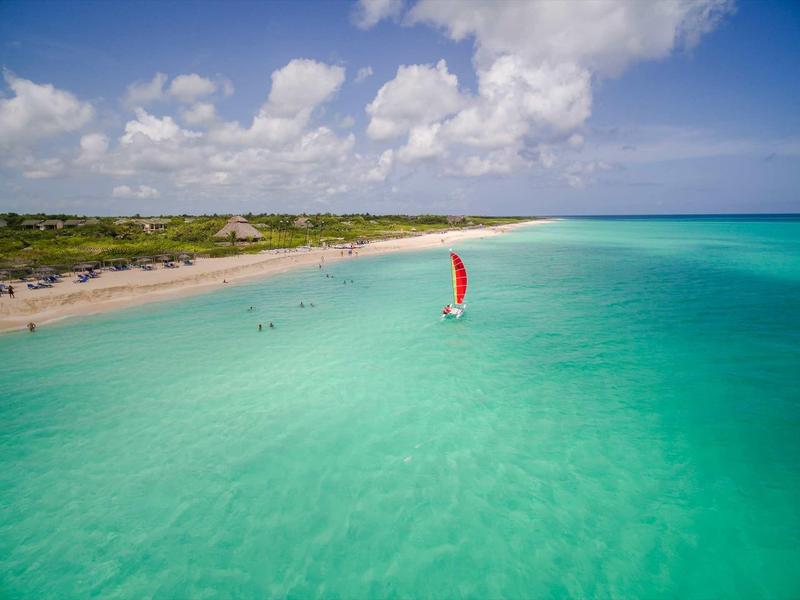 Klarer türkisfarbener Ozean mit Segelboot und Sandstrand unter blauem Himmel mit Wolken.