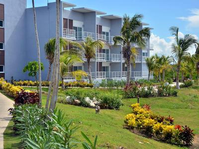 Hotelgebäude mit Balkonen, umgeben von gepflegtem Garten mit Palmen und bunten Blumen.