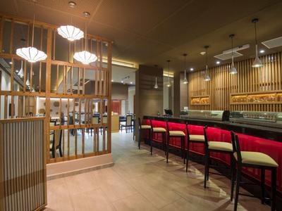 Moderner Hotelbarbereich mit Holzakzenten und roten Barhockern unter warmem Licht.