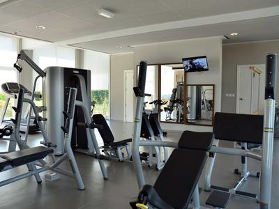 Heller, moderner Fitnessraum mit mehreren Trainingsgeräten und großen Fenstern.