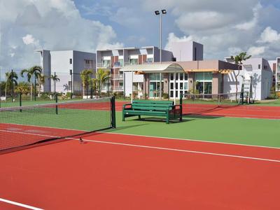 Leerer Tennisplatz vor einem Hotelgebäude mit moderner Architektur und grünen Bänken.