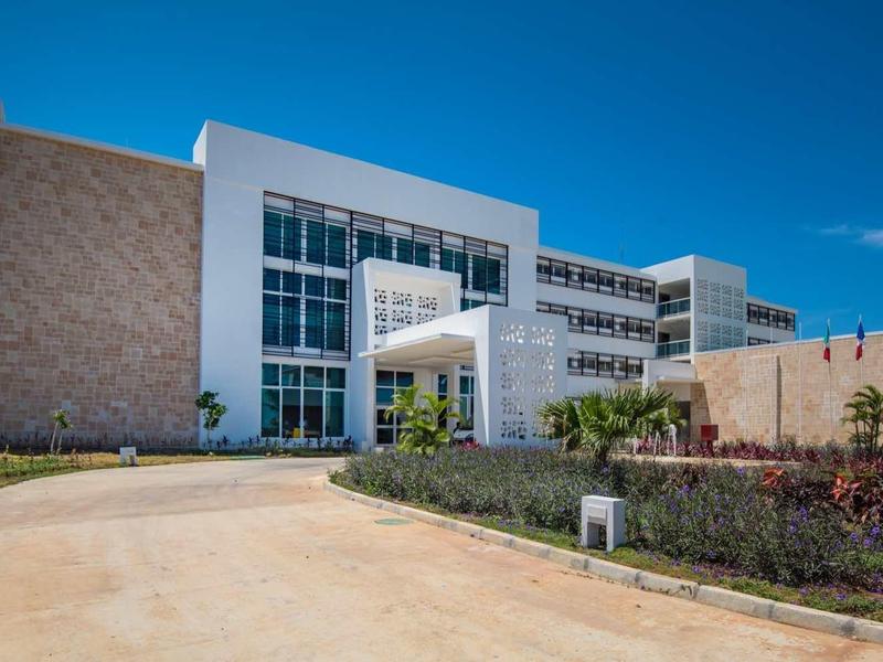 Modernes weißes Bürogebäude mit großen Glasfenstern und gepflegtem Garten unter blauem Himmel.