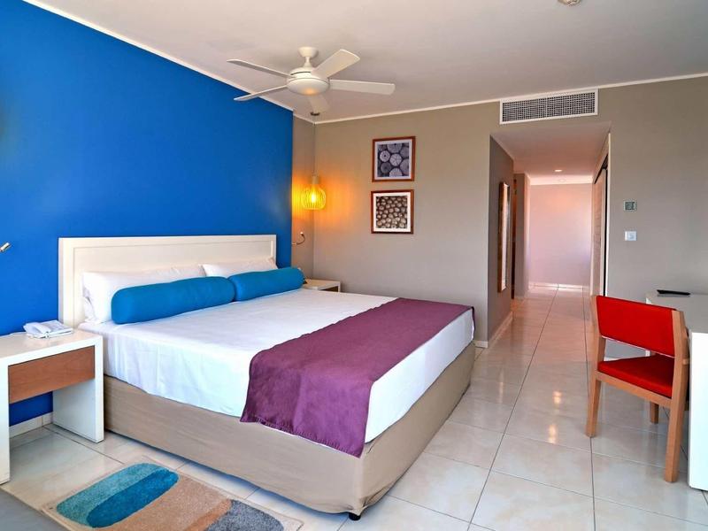 Helles Schlafzimmer mit blau-weißen Wänden, großem Bett, roten Stuhl und minimalistischem Design.