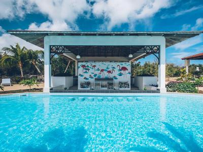 Ein blauer Pool vor einem weißen, offenen Pavillon mit tropischer Umgebung und blauem Himmel.