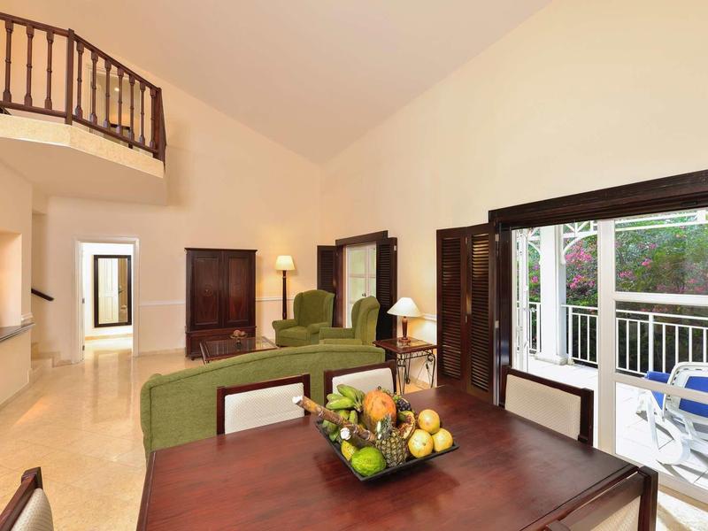 Helles Wohnzimmer mit Holzmöbeln, grünem Sofa, Obstschale auf Tisch und Zugang zur Terrasse.