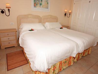 Gemütliches Schlafzimmer mit zwei Einzelbetten, Nachttischen, Wandlampen und heller Gardine.