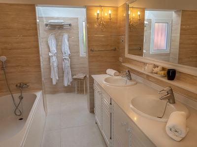 Helles Badezimmer mit zwei Waschbecken, großer Spiegel, Badewanne und Holzverkleidung an der Wand.
