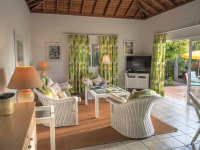 Helles Wohnzimmer mit weißen Möbeln, grünen Vorhängen und Zugang zur Terrasse im Hintergrund.