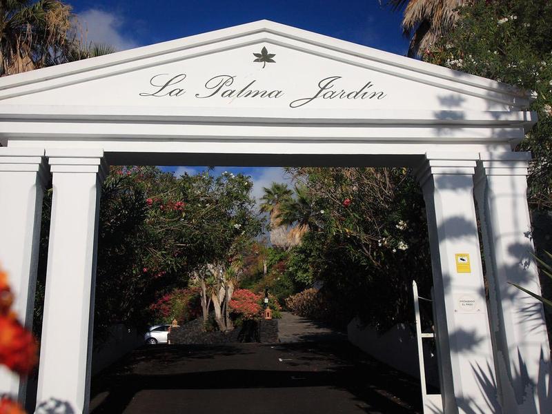 White arched gateway with 'Le Baobab Jacaranda' sign under sunny weather.