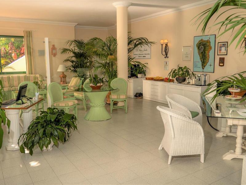 Bright and spacious hotel lounge area with many green plants and white furniture.