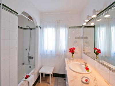 Helles Badezimmer mit weißen Fliesen, großer Spiegel, Dusche, Waschbecken und roten Blumen als Akzent.