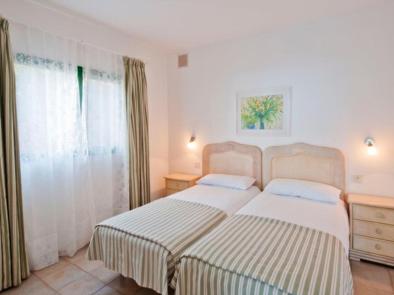 A simply furnished twin room with two single beds, beige curtains, and a small nightstand.