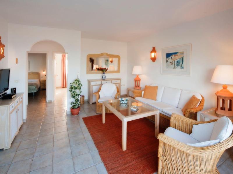 Bright living room with rattan furniture, sofa, rug, and decorations in a hotel room.
