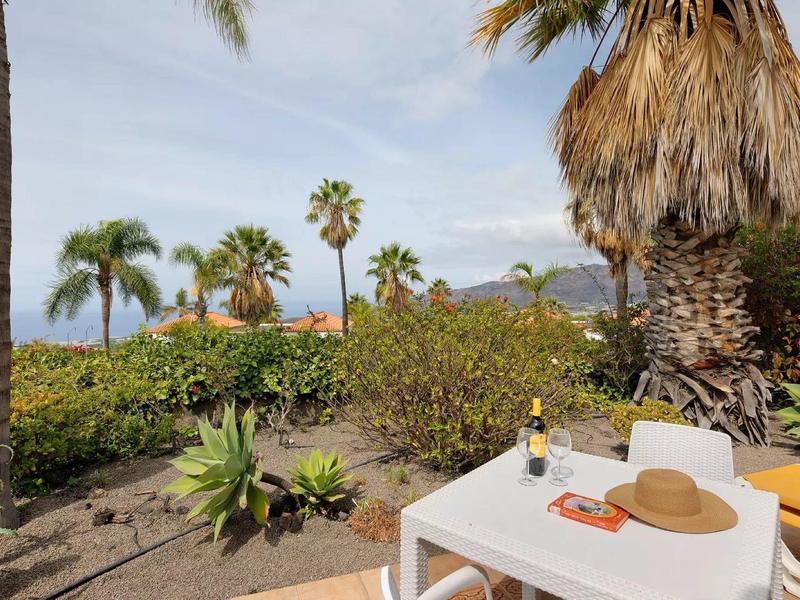 Table with sunhat and drink on terrace overlooking palm trees and mountains.