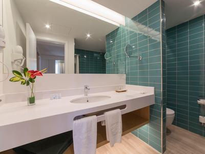 Modernes Badezimmer mit großem Spiegel, weißem Waschbecken, grünen Fliesen und Duschbereich.