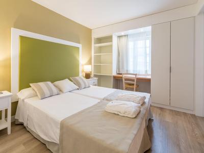 Hell eingerichtetes Schlafzimmer mit großem Bett, grüner Wand, weißen Möbeln und Fenster mit Gardinen.