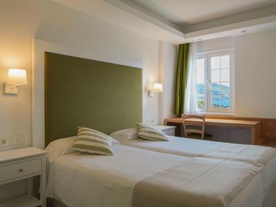 Hell eingerichtetes Schlafzimmer mit zwei Einzelbetten, grünem Kopfteil und Fenster mit Blick.