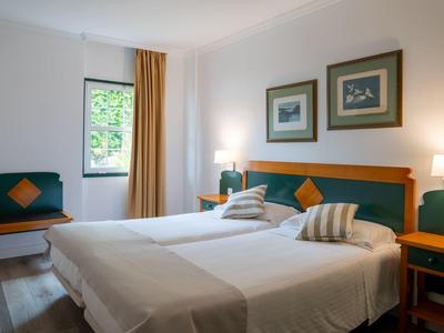Hell eingerichtetes Schlafzimmer mit zwei Einzelbetten, Holzmöbeln und großem Fenster mit Blick.