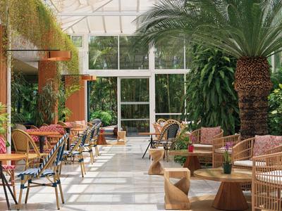 Sala interior luminosa de estilo tropical con palmeras y varias áreas de asientos.