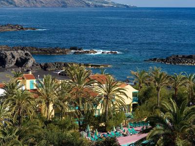 Blick auf tropische Küste mit Palmen, gelbem Gebäude, blauem Pool und türkisfarbenem Meer.