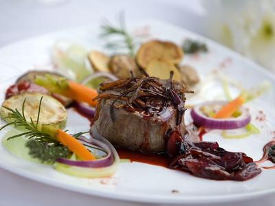 Gegrilltes Steak mit Sauce, gerösteten Kartoffeln, Zwiebeln, Karotten und Kräutern auf weißem Teller.