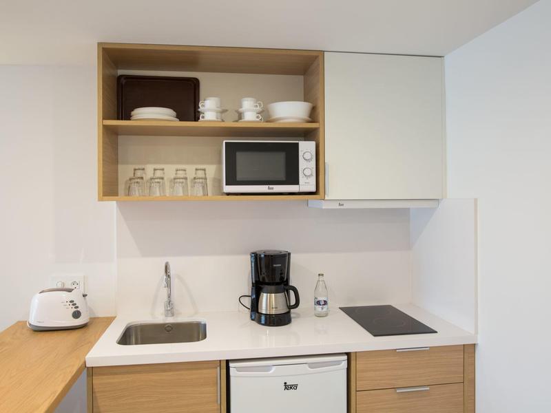 Pequeña cocina moderna con microondas, cafetera, estufa y fregadero en una habitación de hotel.