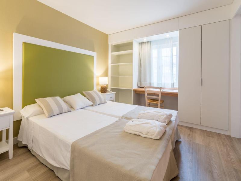 Dormitorio moderno con cama doble, mesitas de noche, armario empotrado y ventana con cortinas.