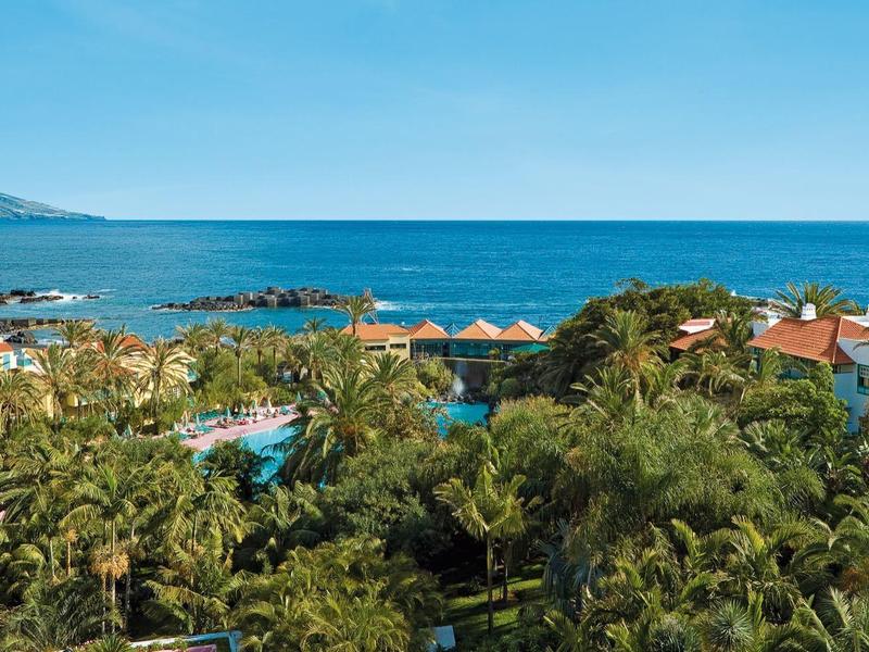 Vista de vegetación tropical, piscina y mar con cielo despejado en la costa.