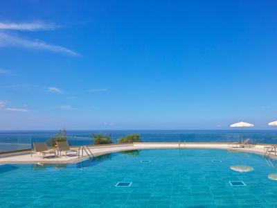 Buitenzwembad met uitzicht op zee onder een blauwe lucht met parasols aan de rand.
