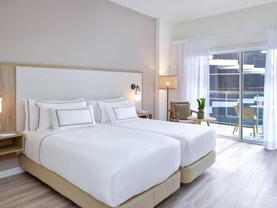 Modern hotelkamer met twee eenpersoonsbedden, lichte houten vloer en balkon met glazen balustrade.