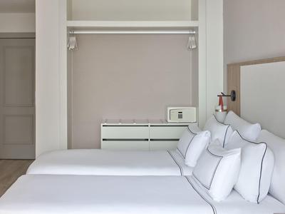 Minimalistische hotelkamer met twee bedden naast elkaar en een open kledingkast.