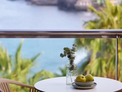 Tafel op balkon met stoel, vaas en citroenen met uitzicht op zee en kliffen op de achtergrond.
