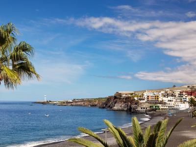 Vista di una località costiera con spiaggia, palme e case sotto un cielo azzurro.