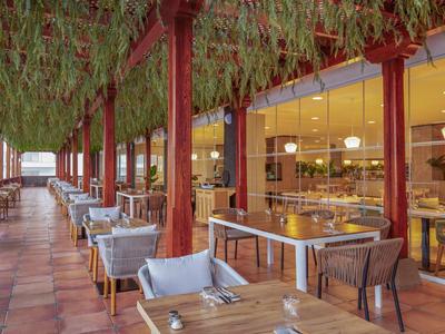 Open eetruimte van hotel met gedekte tafels en groene planten aan het plafond.