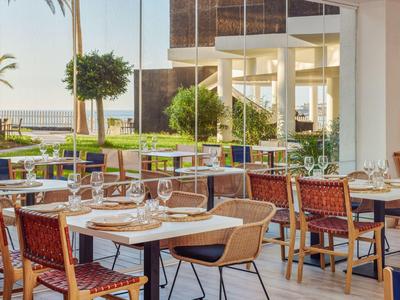 Licht, modern terrasrestaurant met gedekte tafels en uitzicht op de tuin en zee.