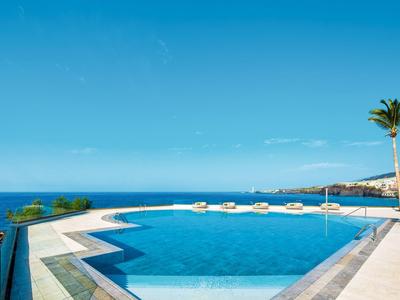 Infinity-Pool mit Meerblick und Sonnenliegen unter klarem blauem Himmel