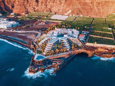 Luchtfoto van een hotel aan een rotsachtige kustlijn met de oceaan erbij bij zonsondergang.