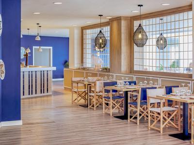 Licht restaurant met houten vloer, blauwe muren, houten stoelen en moderne hanglampen.