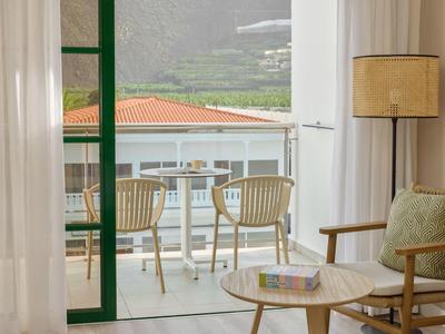 Balkon met stoelen en uitzicht op een gebouw met rode daken, binnen een stoel en tafel.