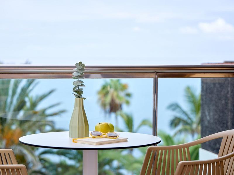 Tavolo moderno sul balcone con vaso, limoni e vista su palme e mare.