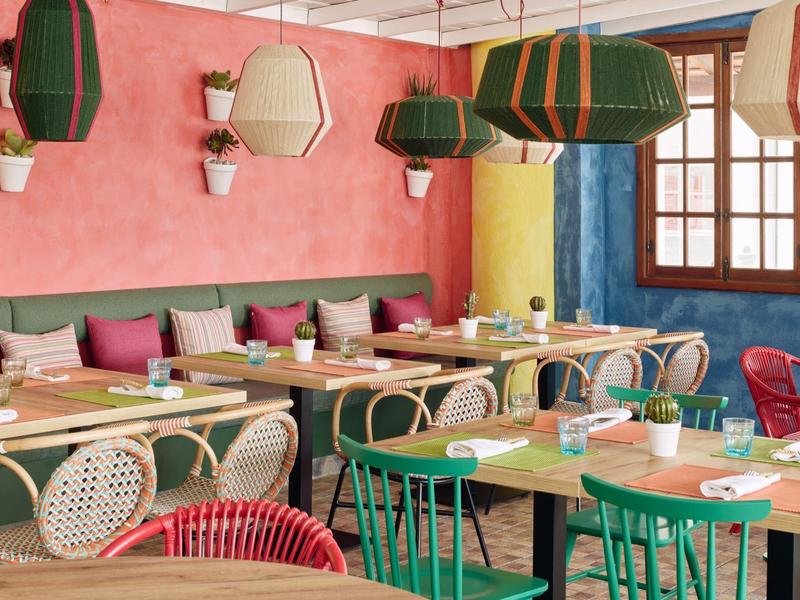 Ristorante decorato con colori vivaci, tavoli in legno e sedie miste di vari colori.