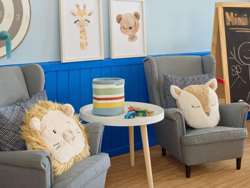 Gezellige zithoek met twee grijze fauteuils, dierenkussens en een klein tafeltje met spelletjes.