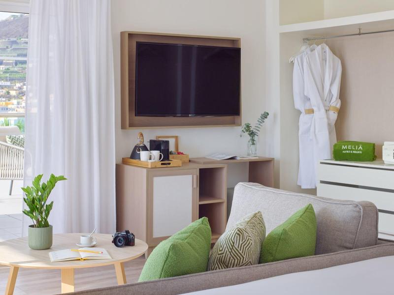 Modern hotelkamer met bank, tv, wit meubilair en balkon met uitzicht op bergen